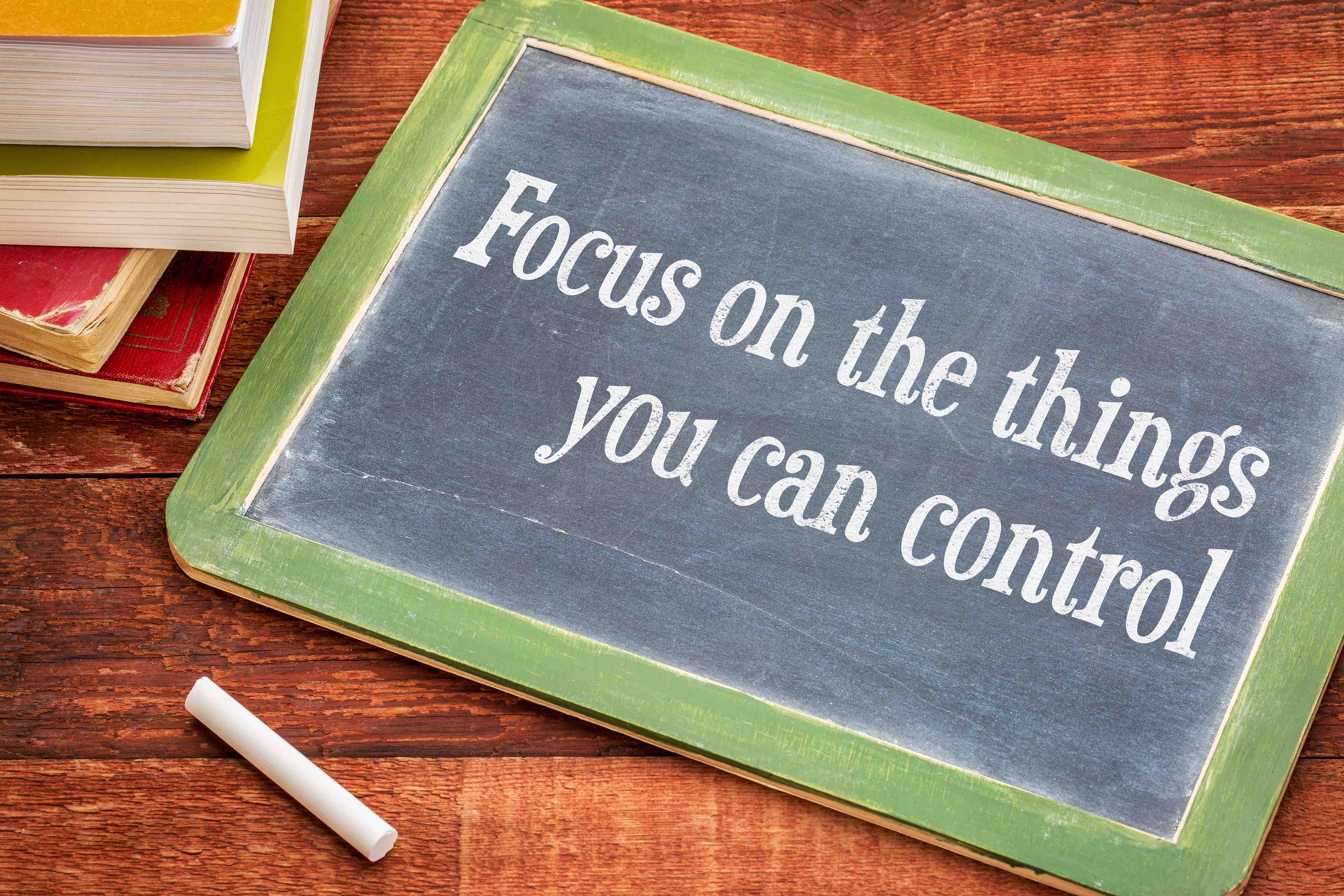 Focus on the things you can control - advice on the slate blackboard with a white chalk and a stack of books against rustic wooden table